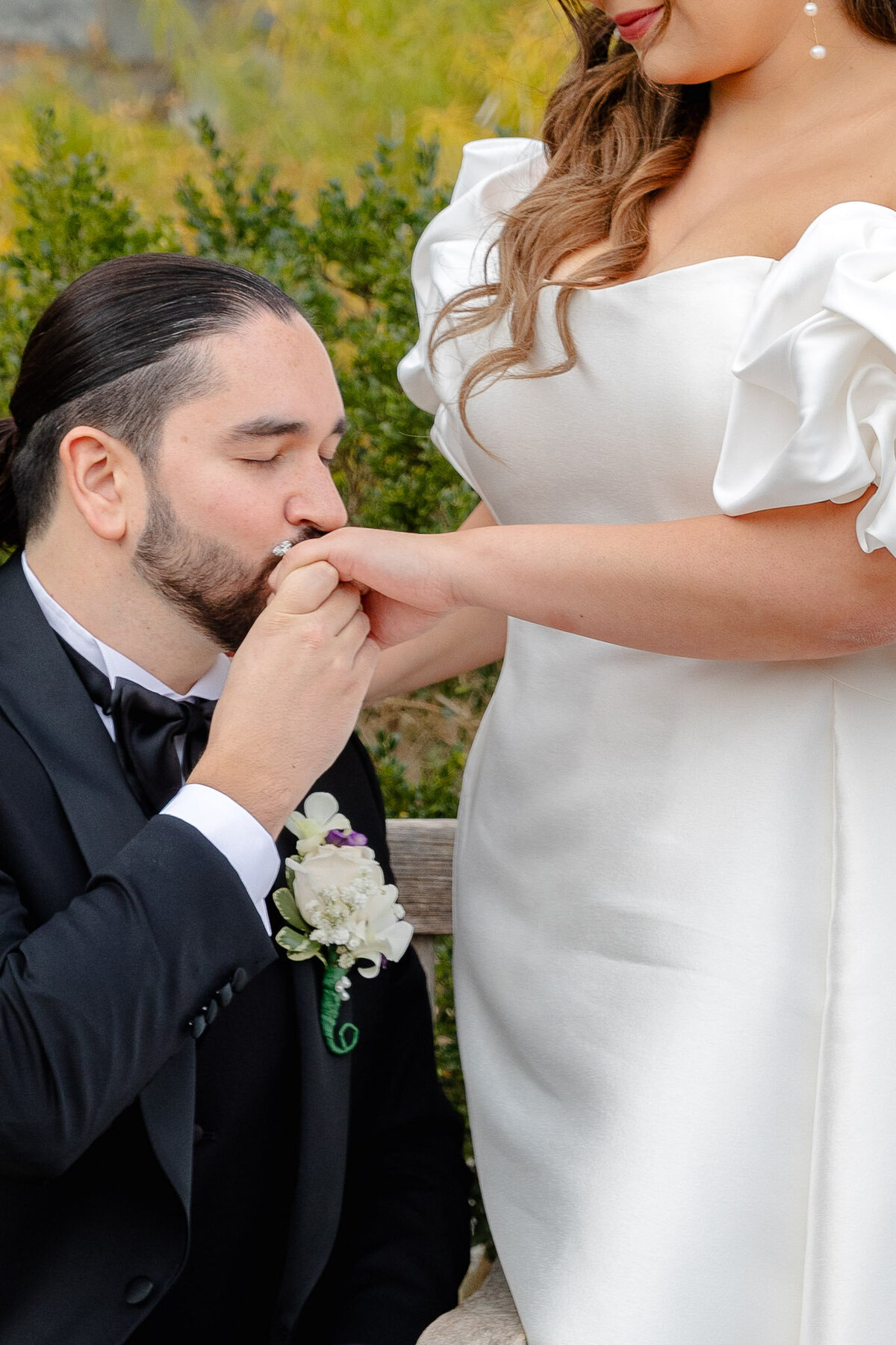 A groom kisses the hand of his bride on their wedding day. The photo is cropped so you can't see her face.