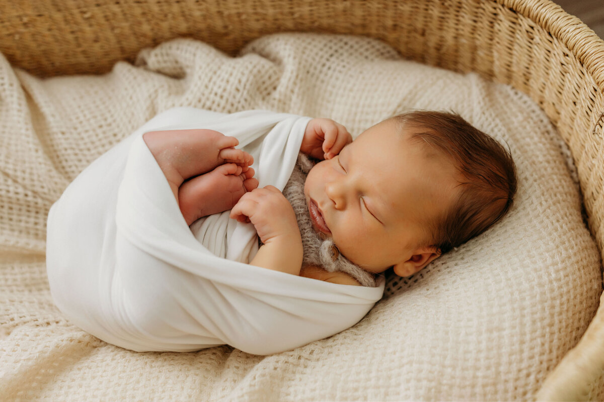 A newborn baby lays swaddled and sleeping in a basket inside his nursery