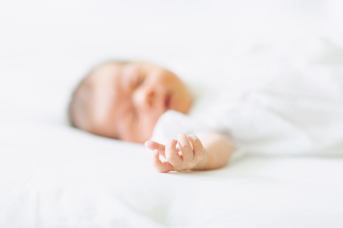 Newborn baby girl sleeping on a bed reaching out her hand