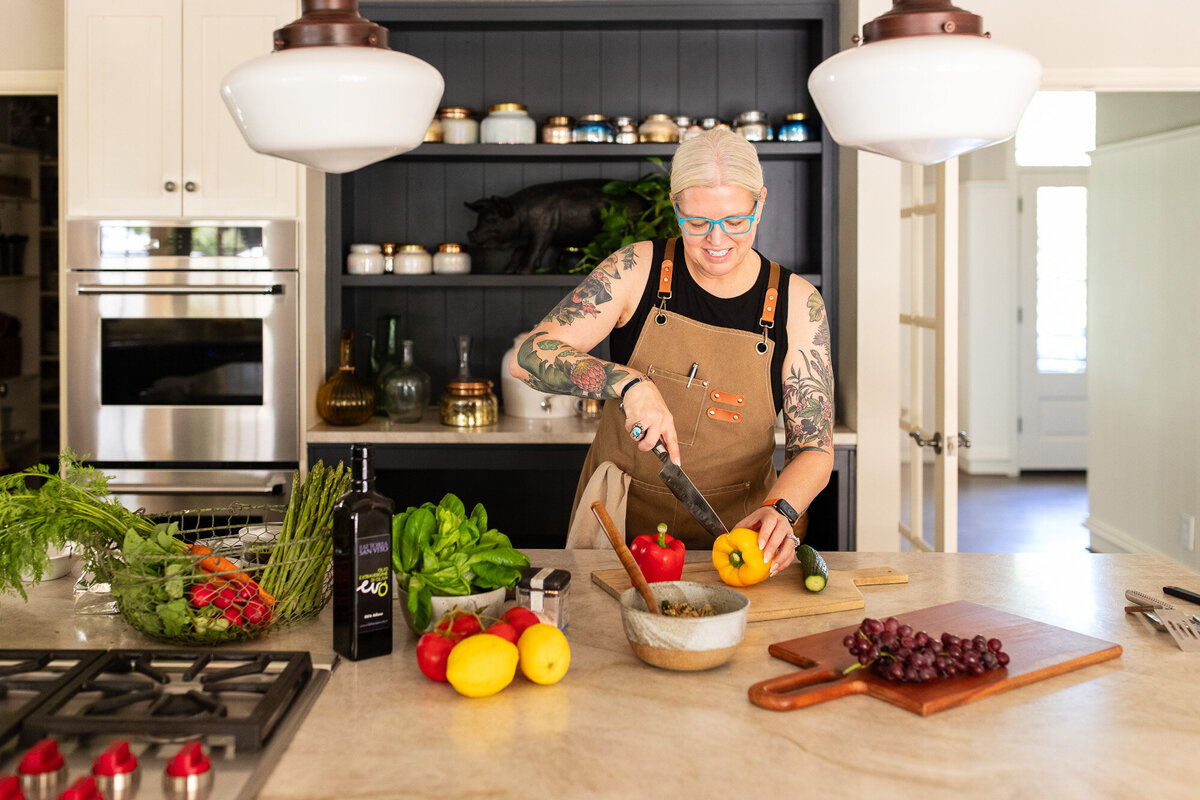 Vegan chef cuts into a yellow pepper in farm house kitchen. 