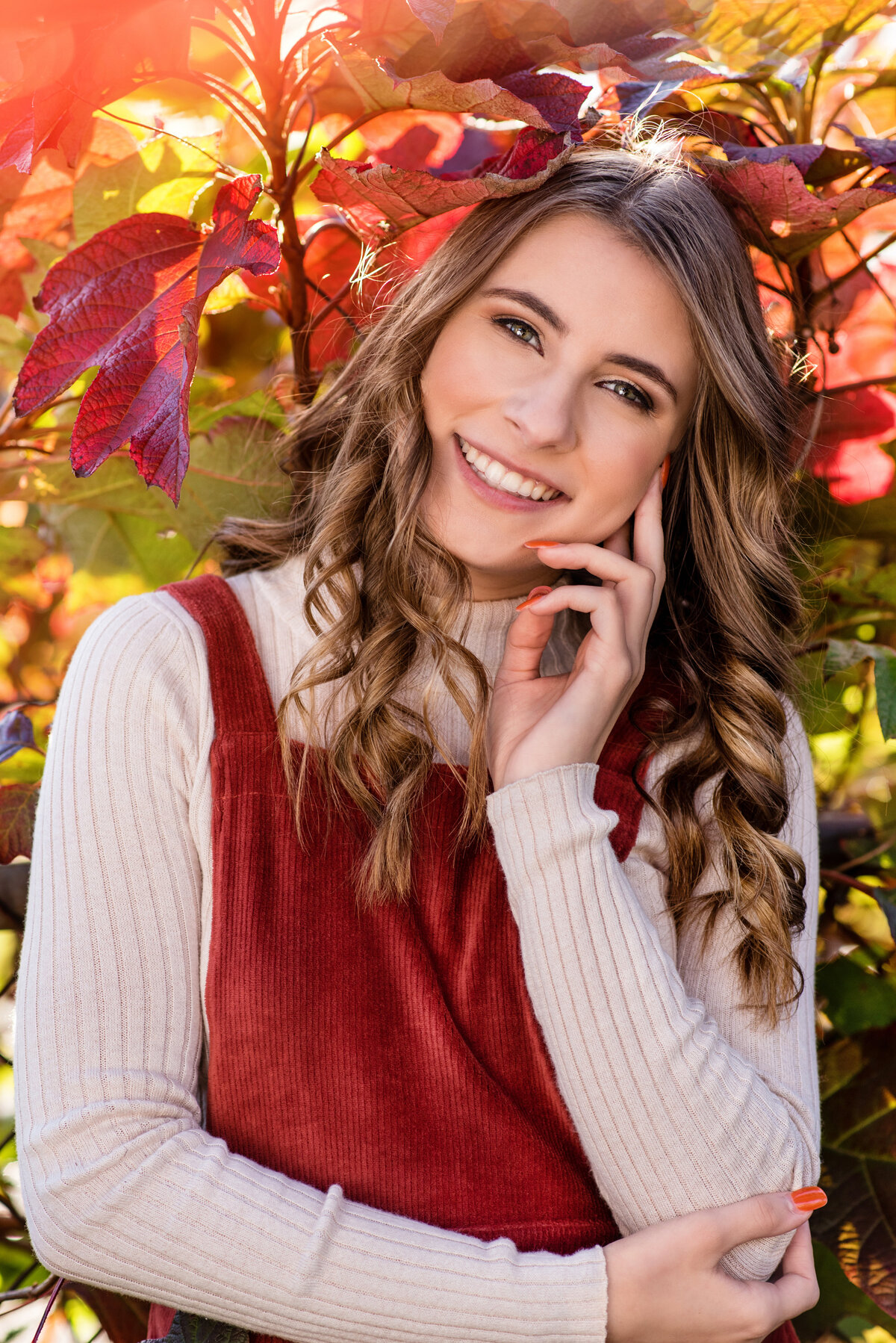 High school senior girl poses for her senior portraits during fall in the colorful leaves.