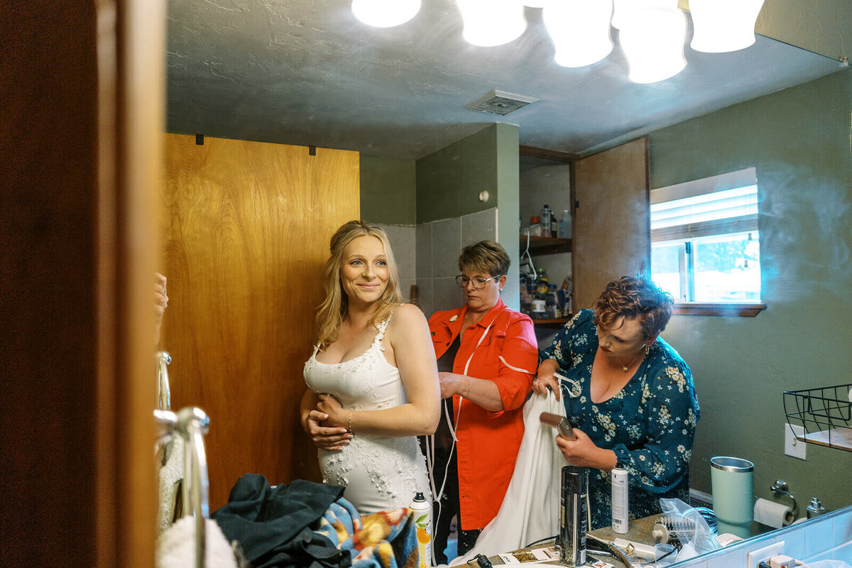 Two people help a bride get ready for her Oregon wedding.