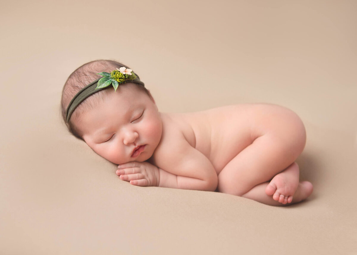 Newborn baby fast asleep curled up with a green headband photographed by Los Angeles newborn photographer Elsie Rose Photography