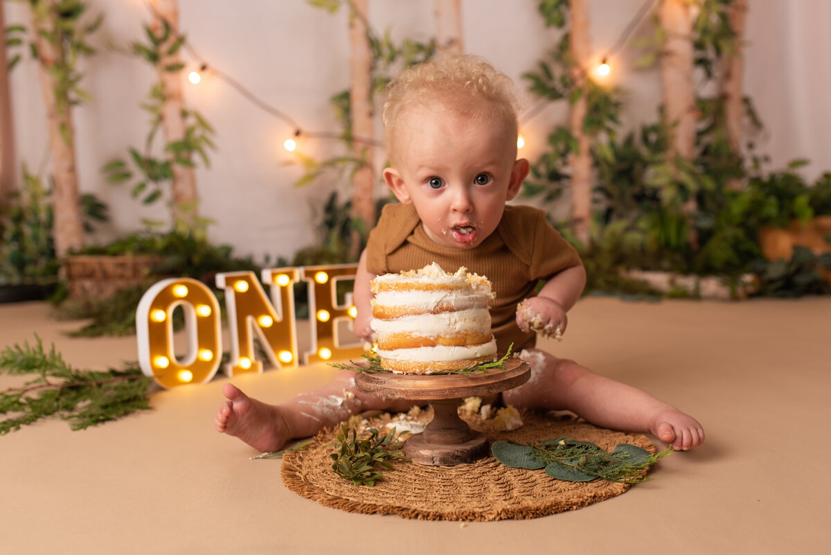 one year old baby boy at marietta ga portrait studio eating smash cake in a forest themed set up