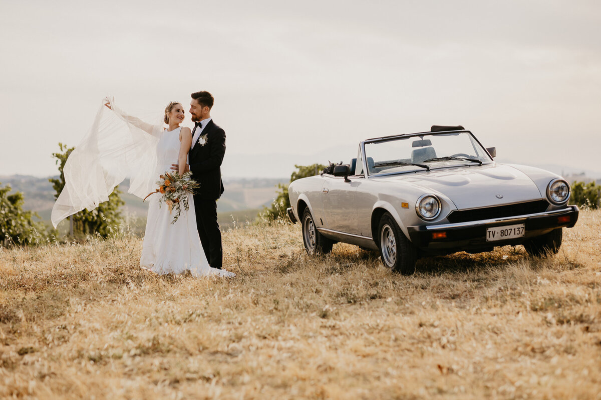Bride and groom with vintage silver car in vineyards near Villa Dianella, romantic Tuscany wedding photographer.