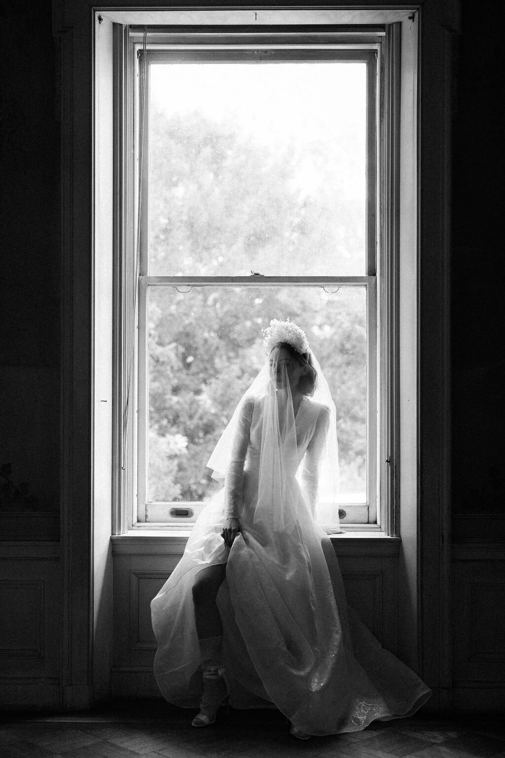 bride in wedding dress sitting on window  sill