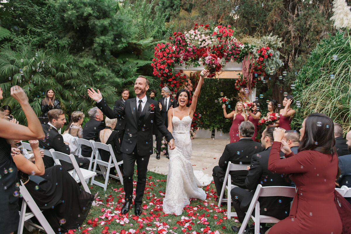 A joyful moment capture by Los Angeles Wedding Photographer, at Hotel Bel Air of the bride and groom walking down the aisle, while their guests are blowing bubbles. 