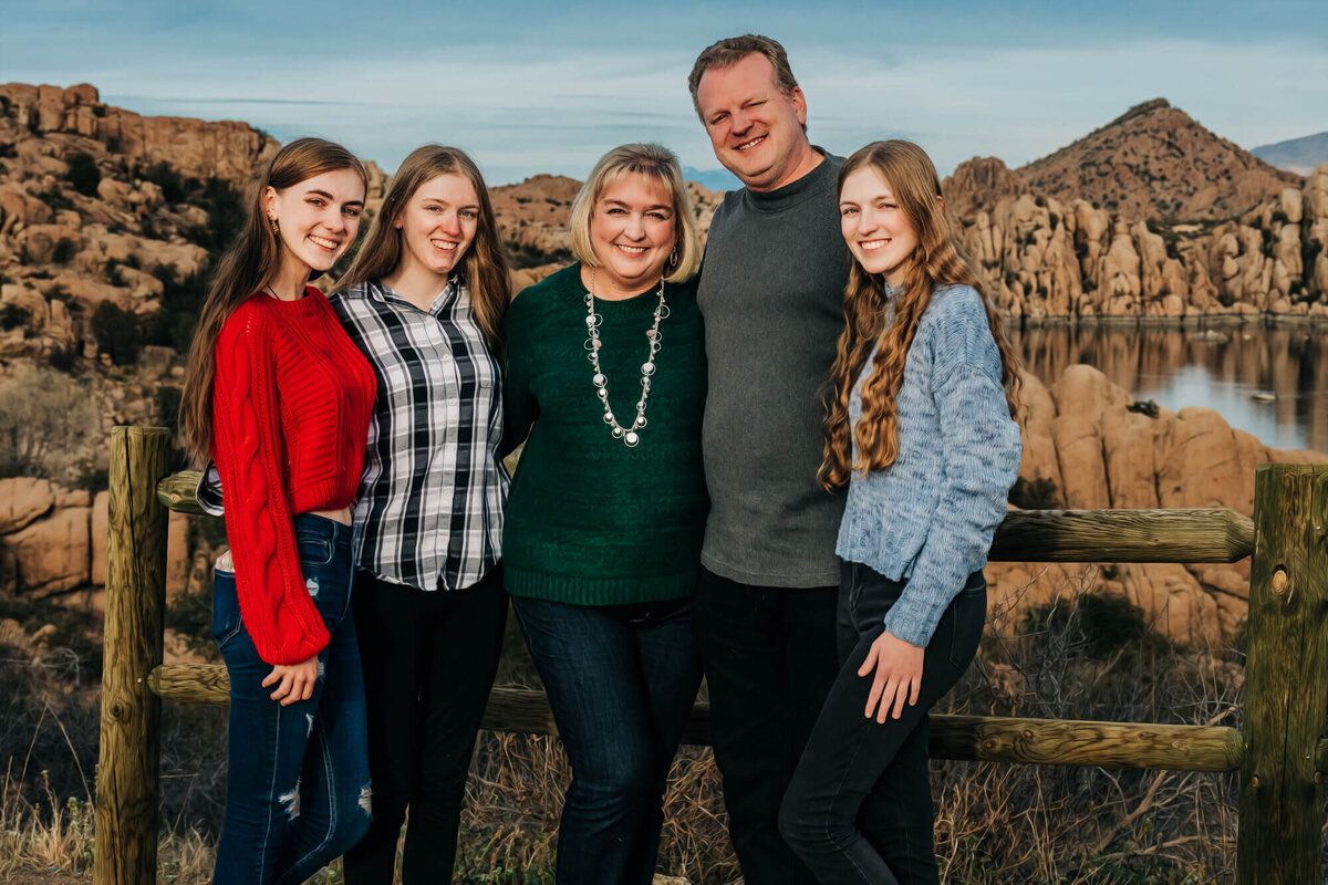 Family stands in front of fence above Watson Lake for Prescott family photographer Melissa Byrne