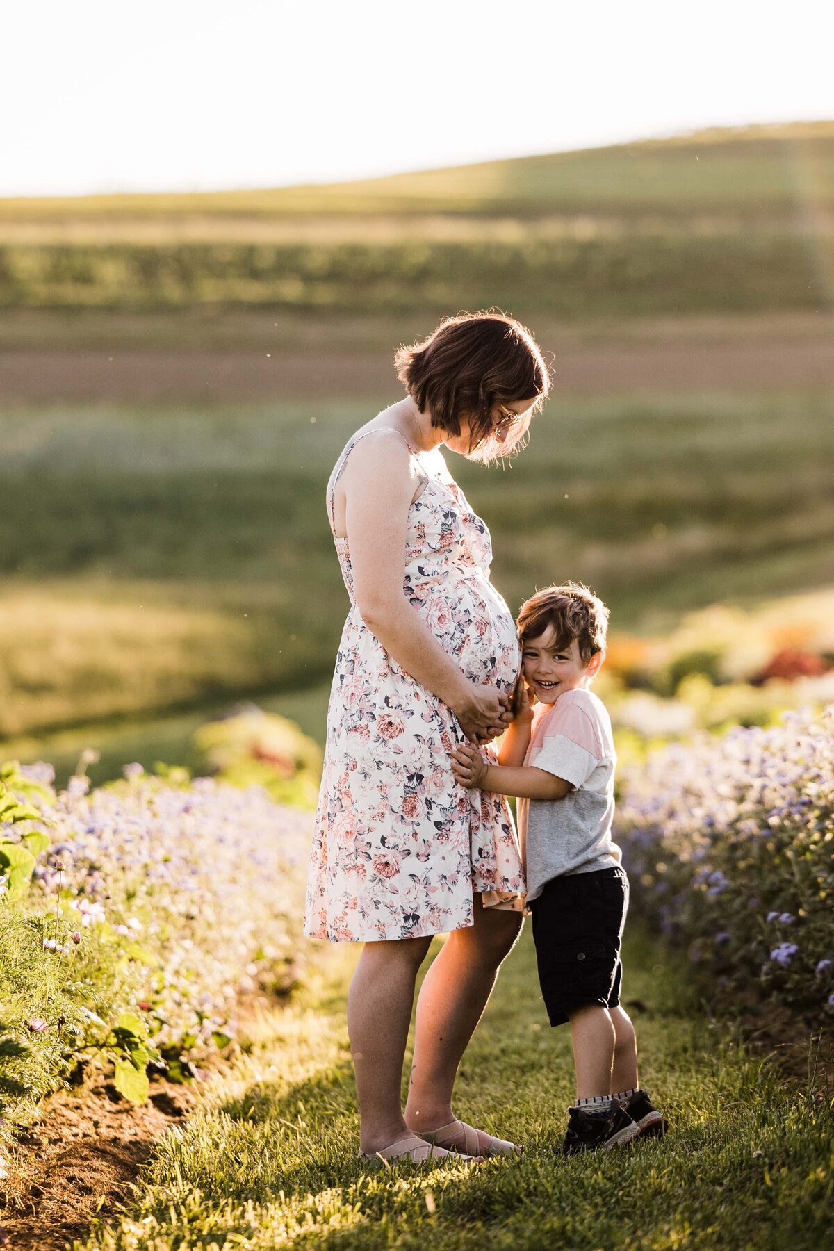 A pregnant woman standing in a field with a young boy hugging her belly, captured beautifully by a Pittsburgh maternity photographer.
