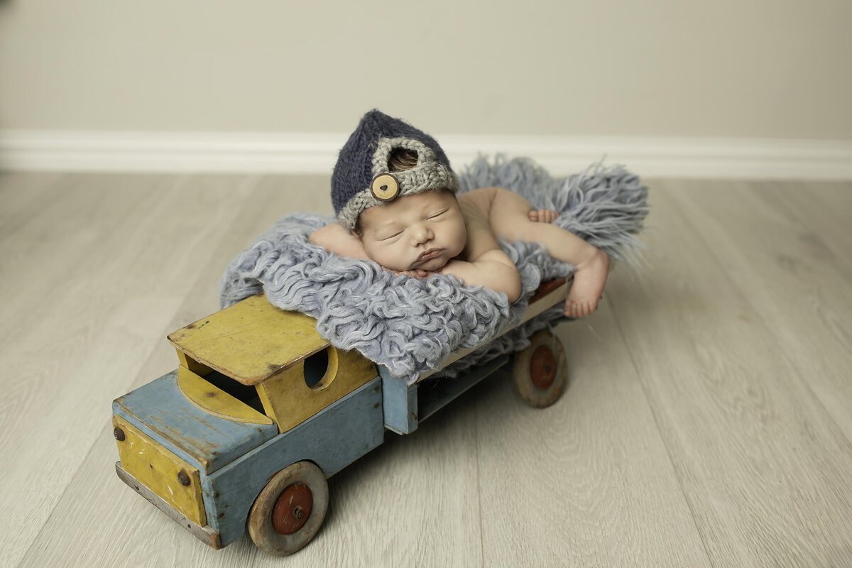 Newborn baby boy peacefully lying in a truck prop, wearing a tiny hat, creating a charming and rustic scene