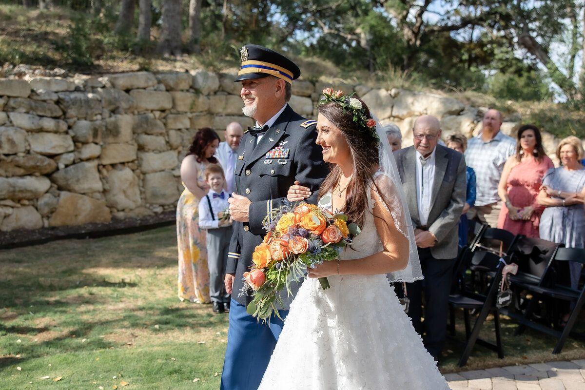 bride with orange flowers walks arm in arm with father in military uniform at Hayes Hollow at Hidden Falls wedding in Spring Branch Texas