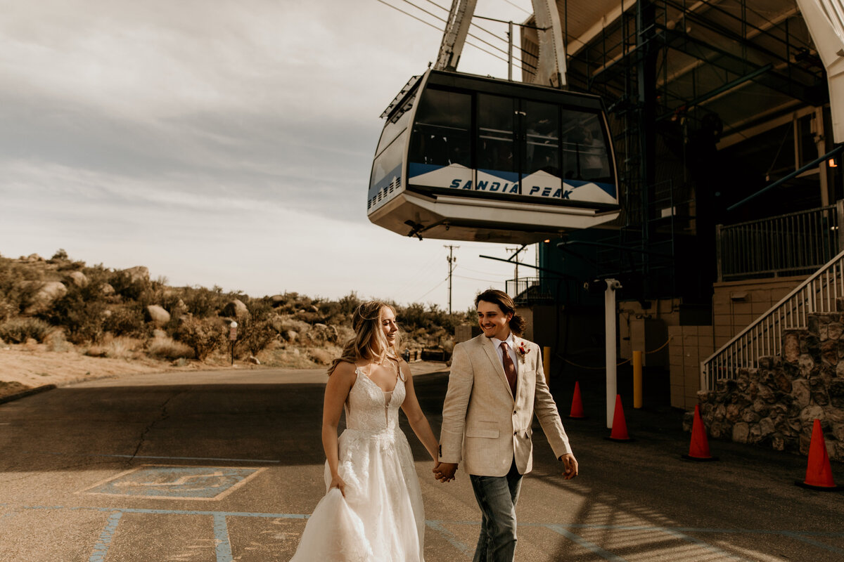 bride and groom walking together with sandia peak tram above them