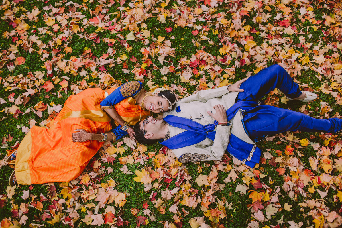 A bride and groom laughing while laying on the fall leaves during the wedding at the red maple vineyard in poughkeepsie, ny