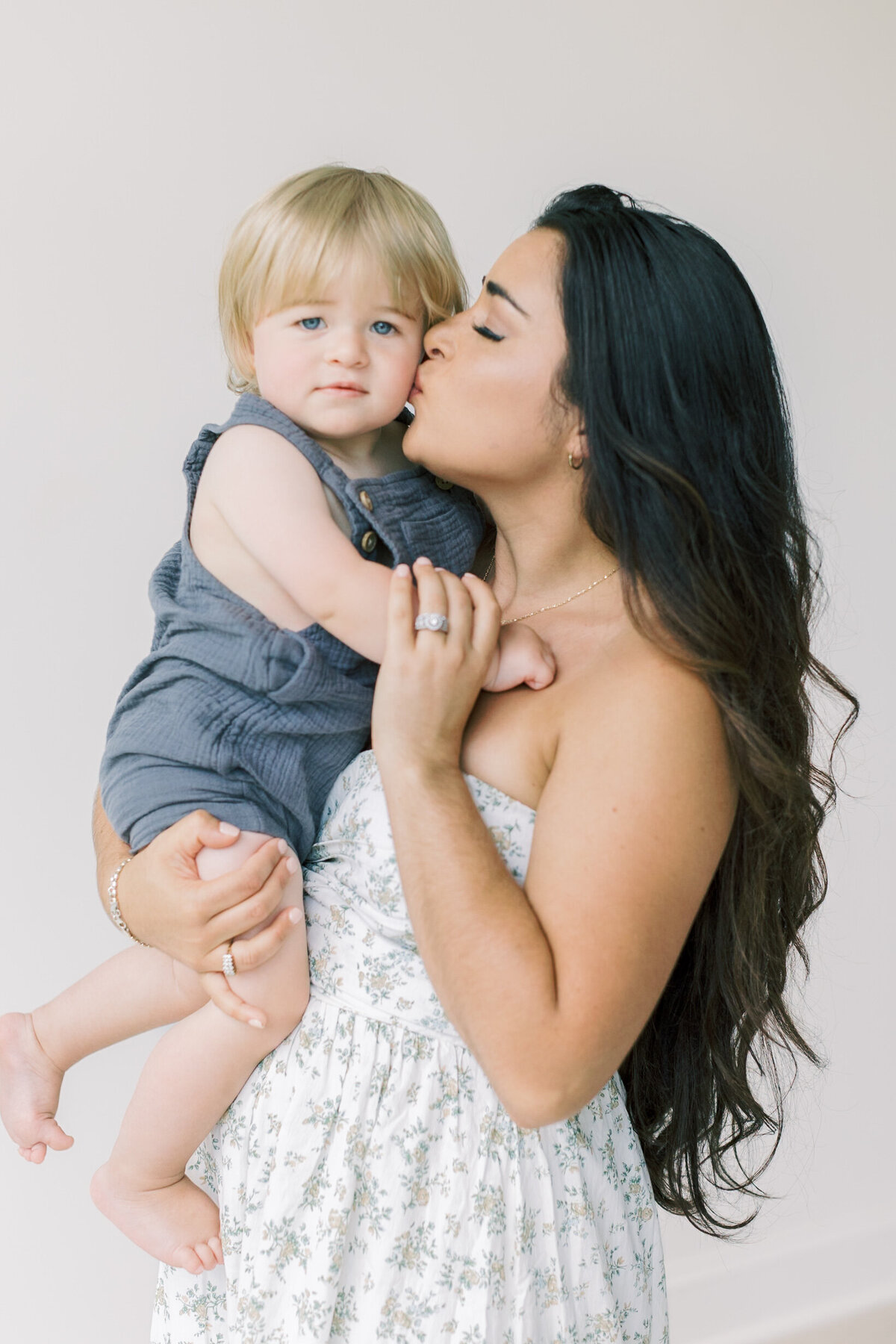 A loving mother kissing her baby boy’s cheek during a cozy studio session filled with natural light — Raleigh portrait photographer.