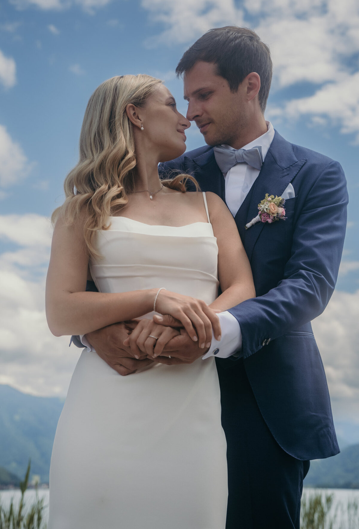 Wedding couple stands close under a blue sky during romantic couple session.