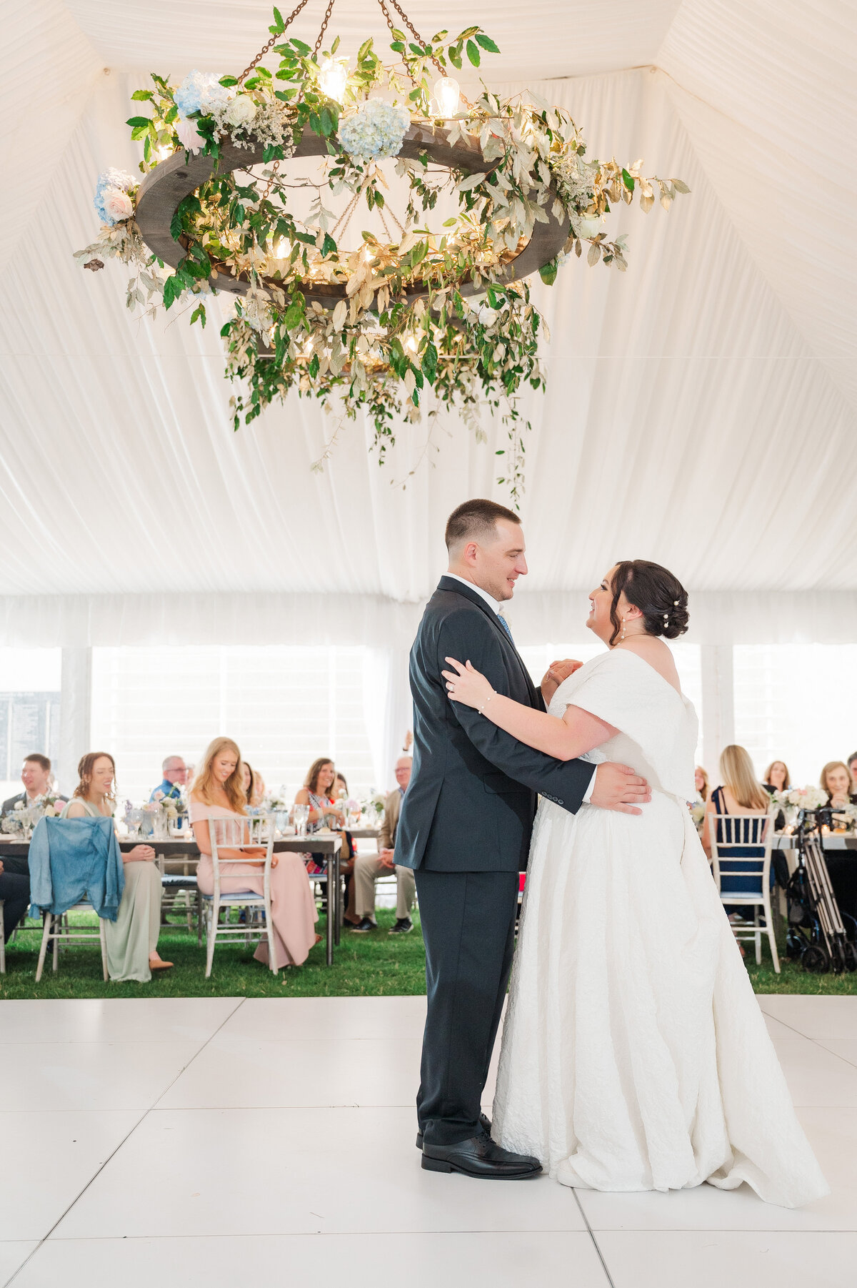 wedding couple dancing their first dance in the reception tent at Frick Museum with a chandelier of flowers designed by the fox and the fleur florist