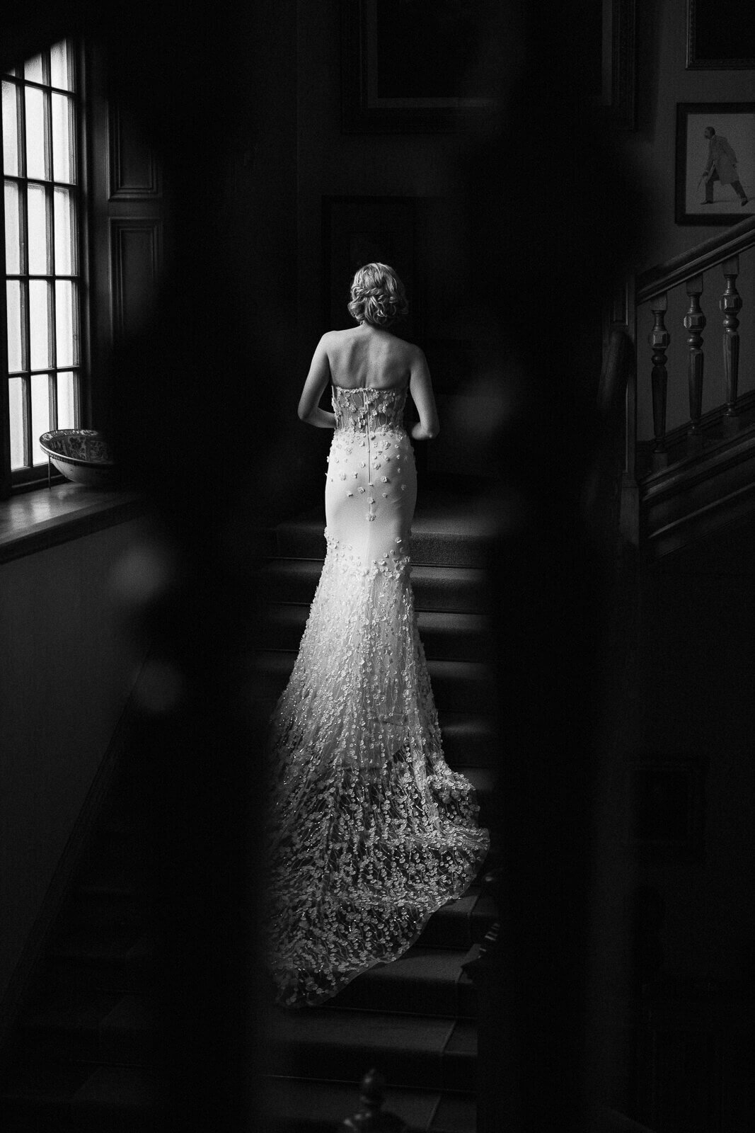 Glamorous bride walks up the stairs in a stately home, her long dress trails behind her.