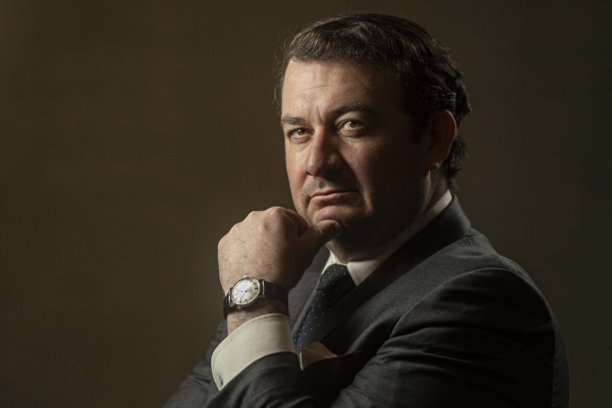 Headshot in CT of man in dark suit smiling confidently, hand on chin, with warm lighting by Rob Faber Photography.