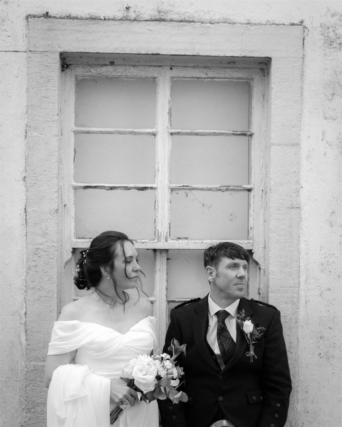 A couple lean against a window on their wedding day