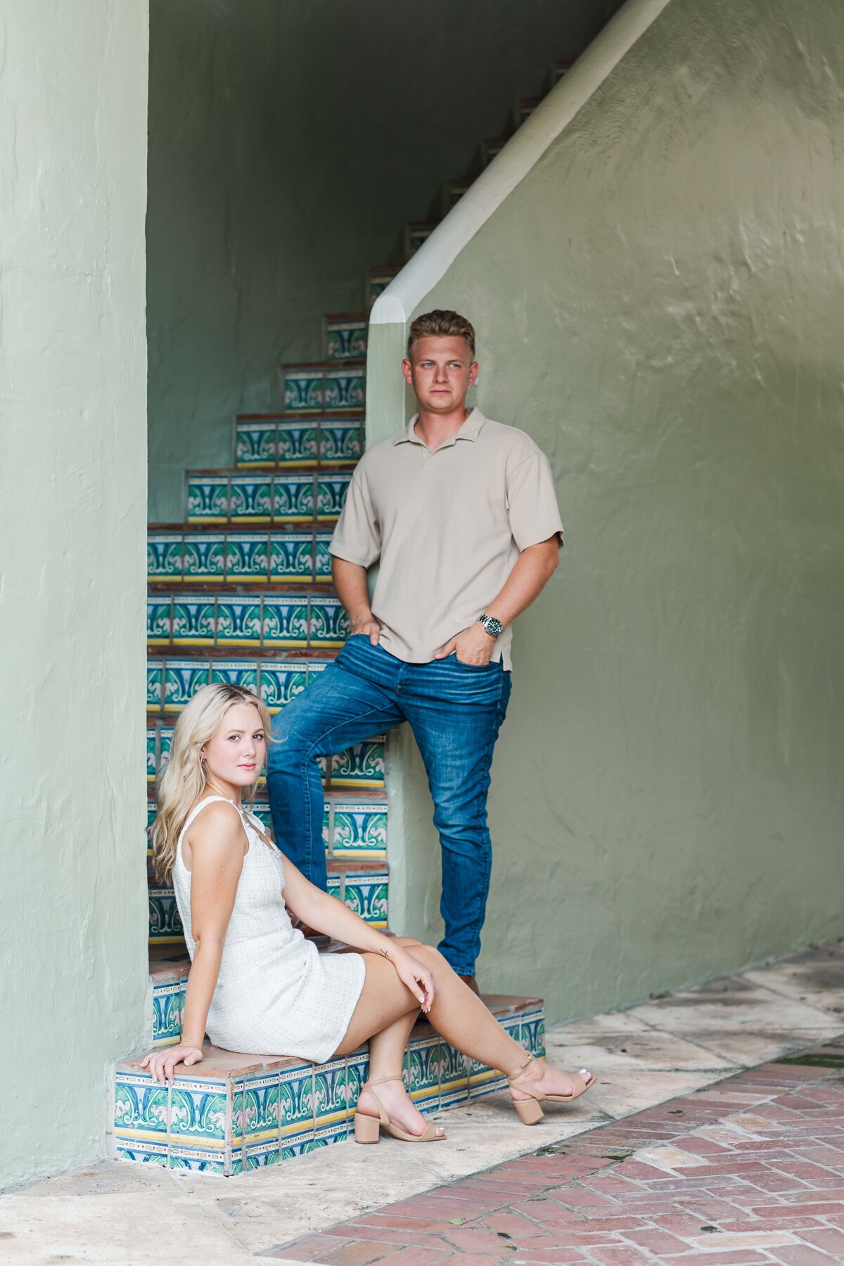 a couple looking at the camera, she is sitting down and he is standing next to her