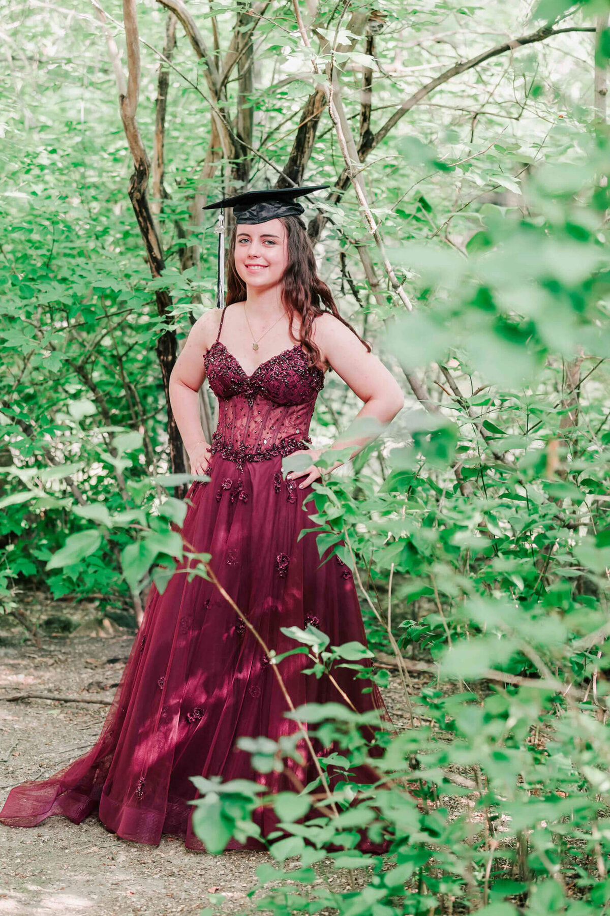 Standing in an alcove of trees wearing her grad cap. 