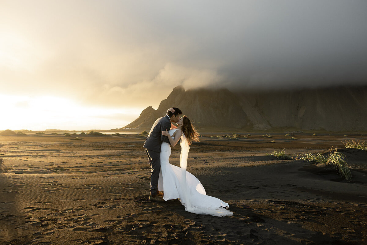 Couple kissing at sunset on the black sand beach in Iceland with dramatic mountains, photographed by a destination elopement photographer.