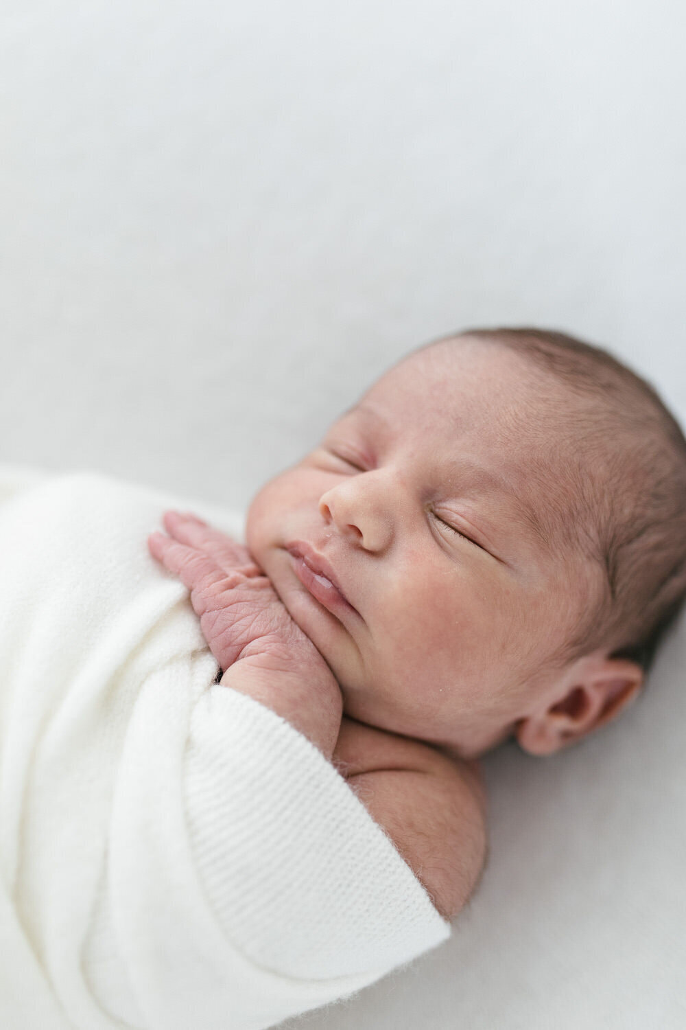 Newborn baby is asleep on the bed with thier hand tucked under thier chin