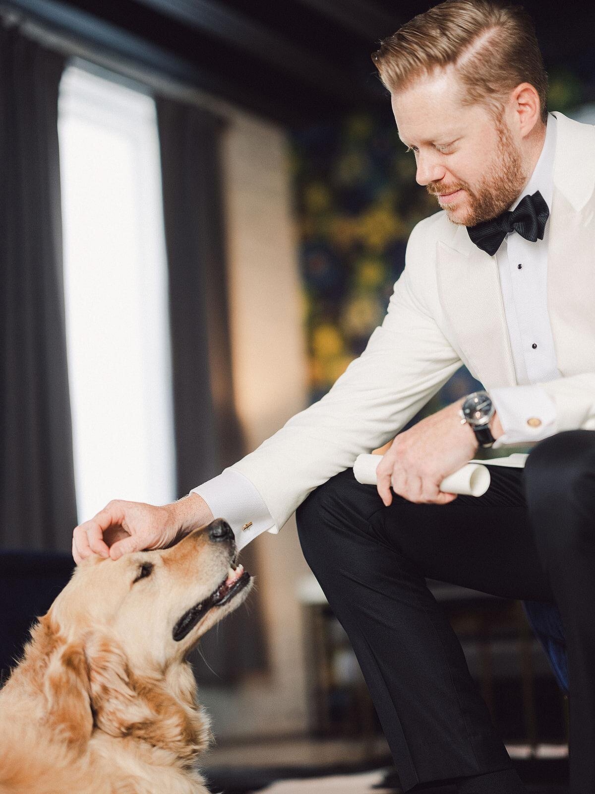 The groom, wearing a tuxedo with a white jacket pet his golden retriever  Frank, who is also the best man at his wedding