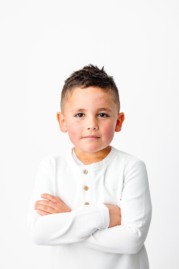 Little boy folds arms in a white studio.