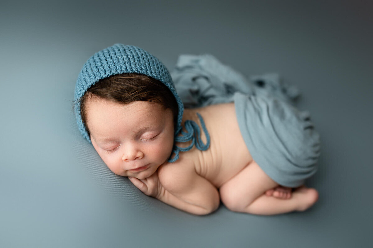Newborn boy posed on a blue background.