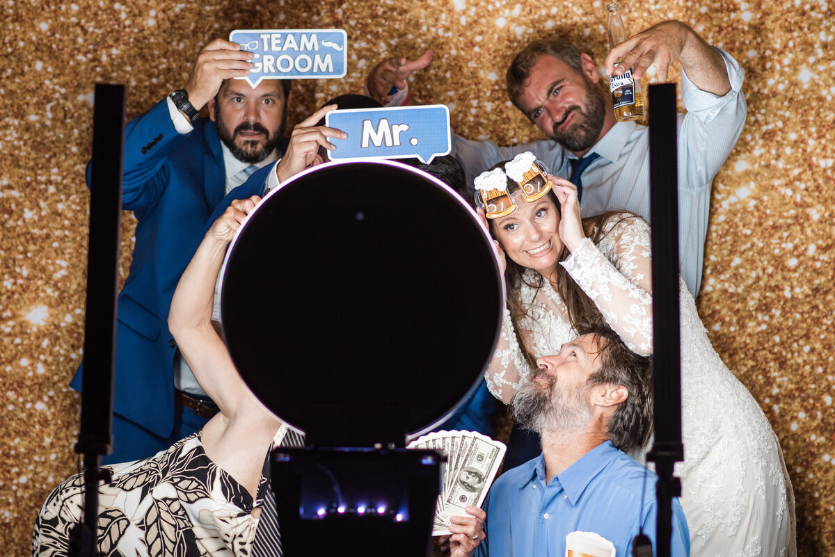 bride and groom pose with guests in photo booth