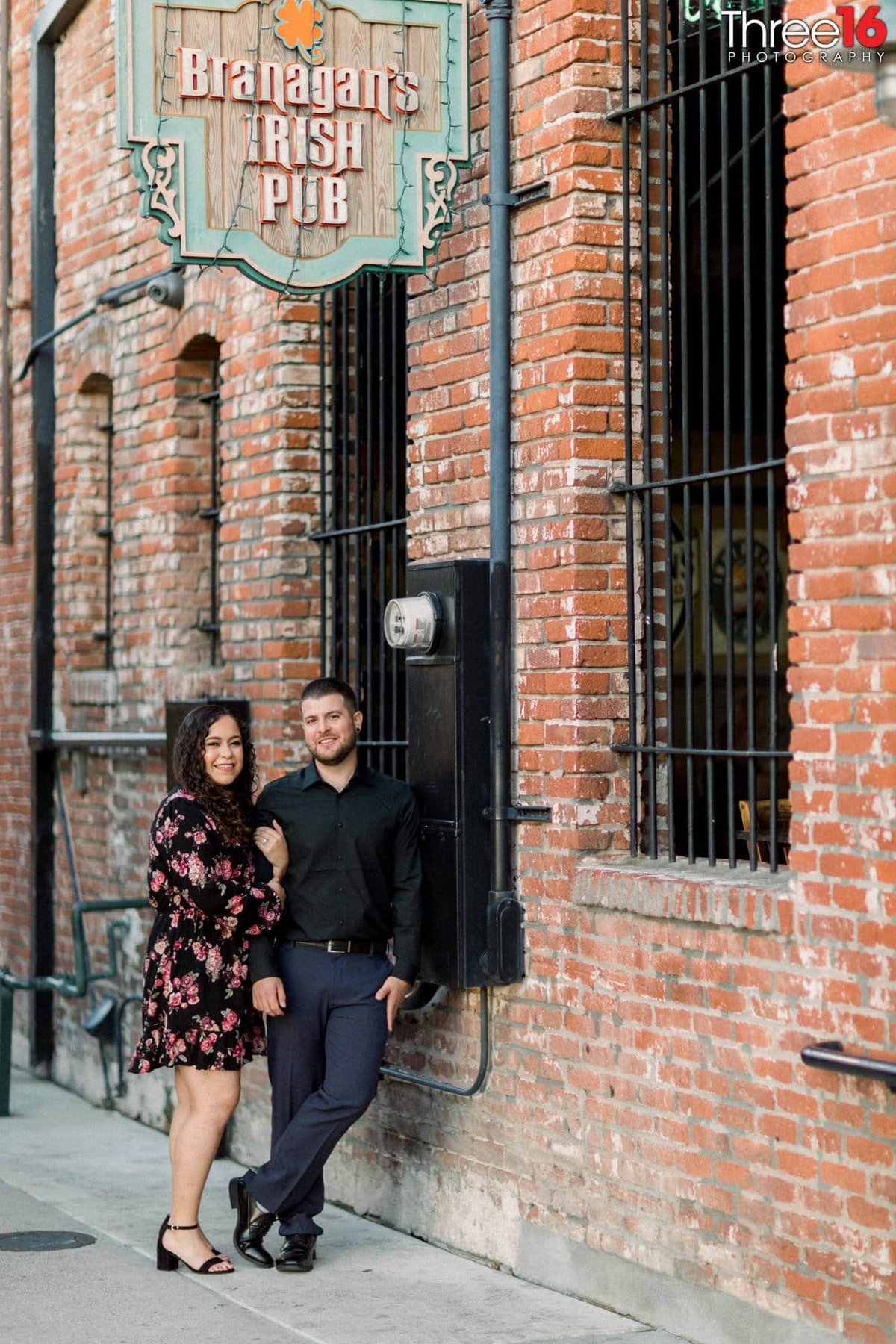 Engaged couple pose together against a brick wall in the back alley of downtown Fullerton