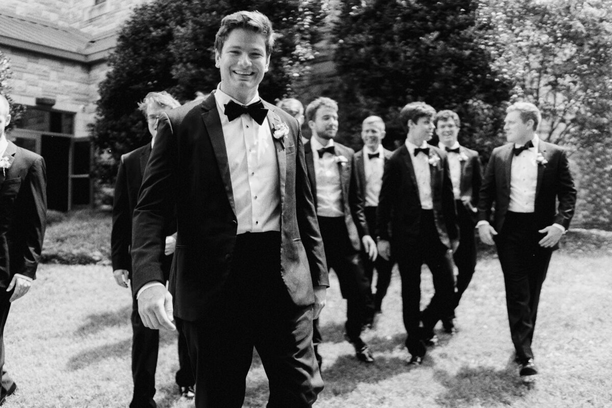 A happy groom walking with his groomsmen during a garden wedding 