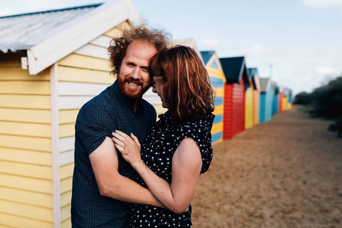 Couple embracing outside Brighton Beach bathing boxes, couple photoshoot Melbourne, And So I Don't Forget Photography