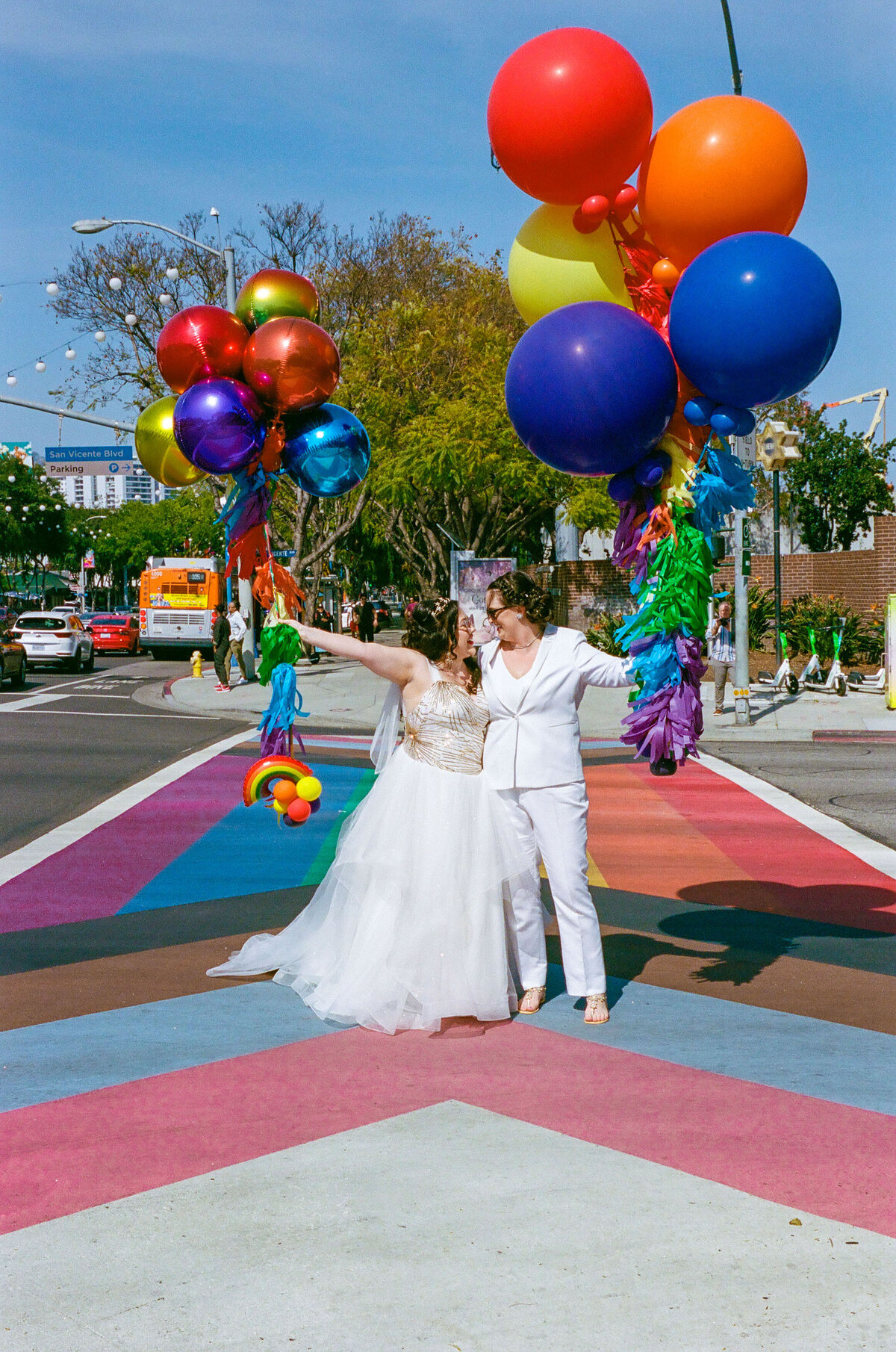 A wedding couple holding balloons while standing on a rainbow crosswalk.
