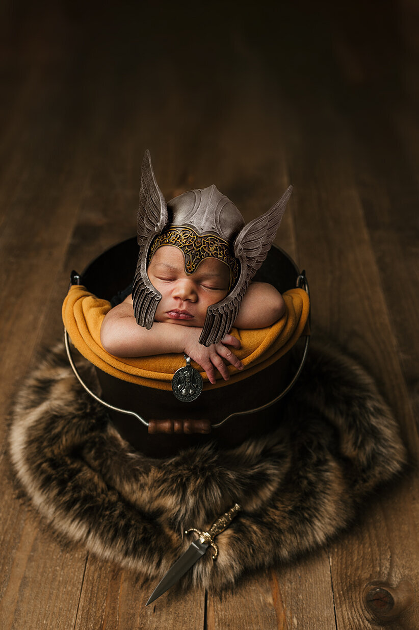 Sleeping baby in a bucket with a viking helmet on surrounded by fur