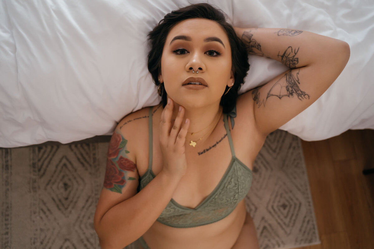 Woman with tattoos looking into te camera serenely in boudoir portrait