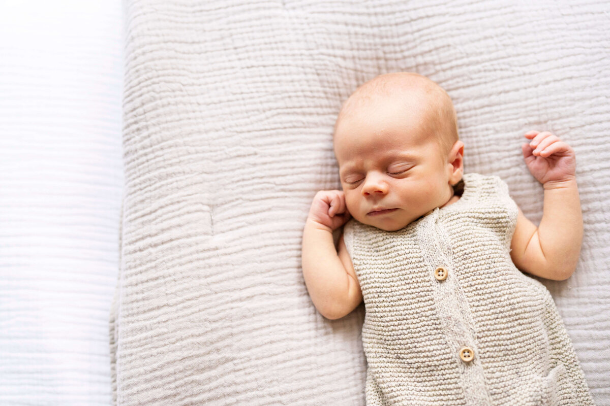 Newborn baby on bed in tan knit oufit