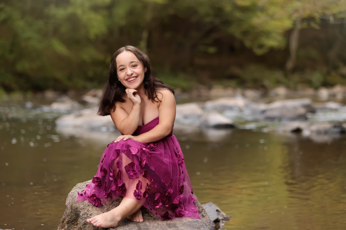 Senior sitting on a rock in the river in Durham wearing a beautiful dress.