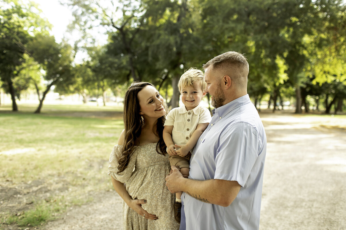 A heartwarming maternity photo at Trinity Park, with mom lovingly hugging big brother while dad holds him in his arms, capturing a tender family moment as they anticipate the new arrival, beautifully captured by Chunky Monkey Photography.