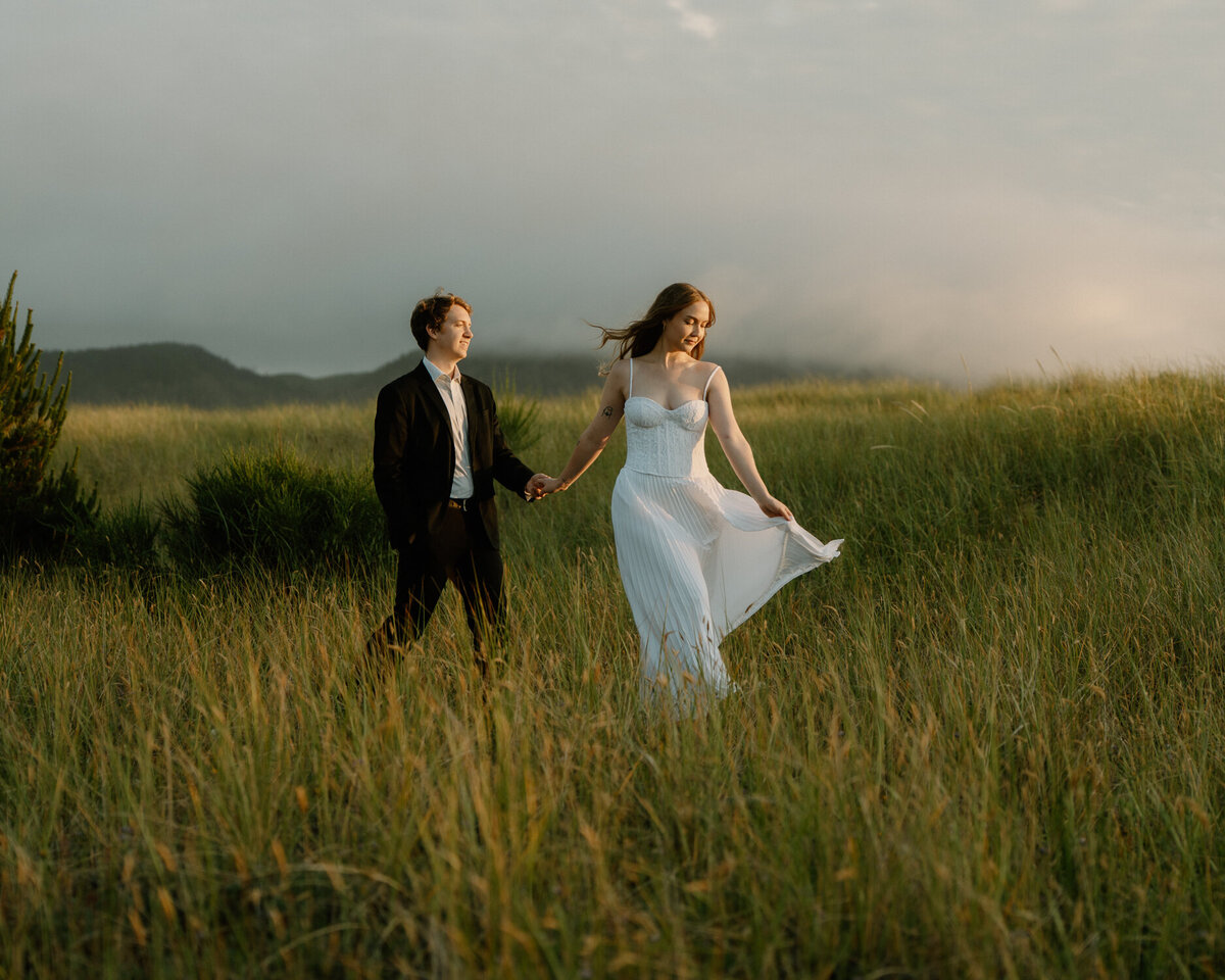 A bridal couple runs through green grass during sunset for their Seaside, Oregon elopement. 