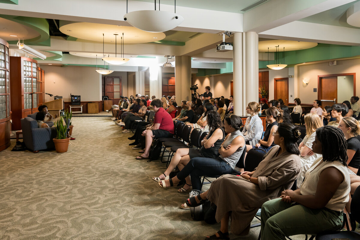 a group of people sit and watch a panel of speakers