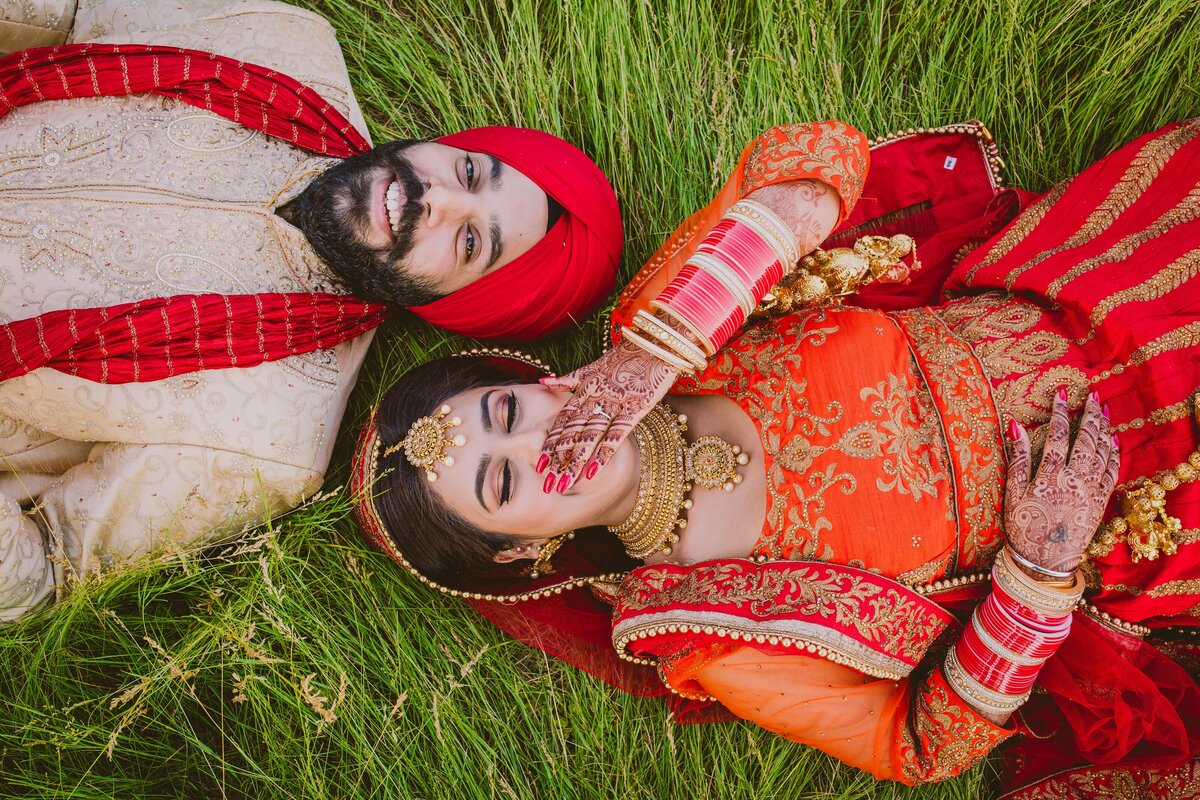 sikh bride and groom laying on the grass sharing a laugh on their wedding day