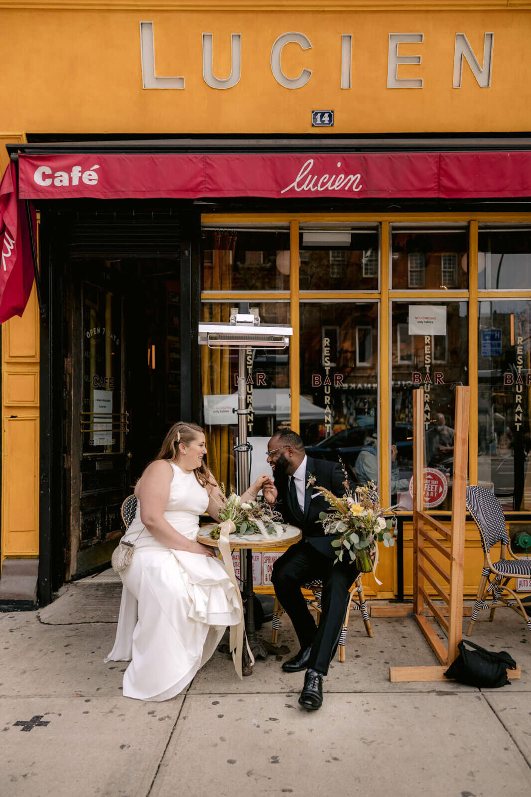 The bride and the groom are sitting outside Lucien Cafe in New York City.