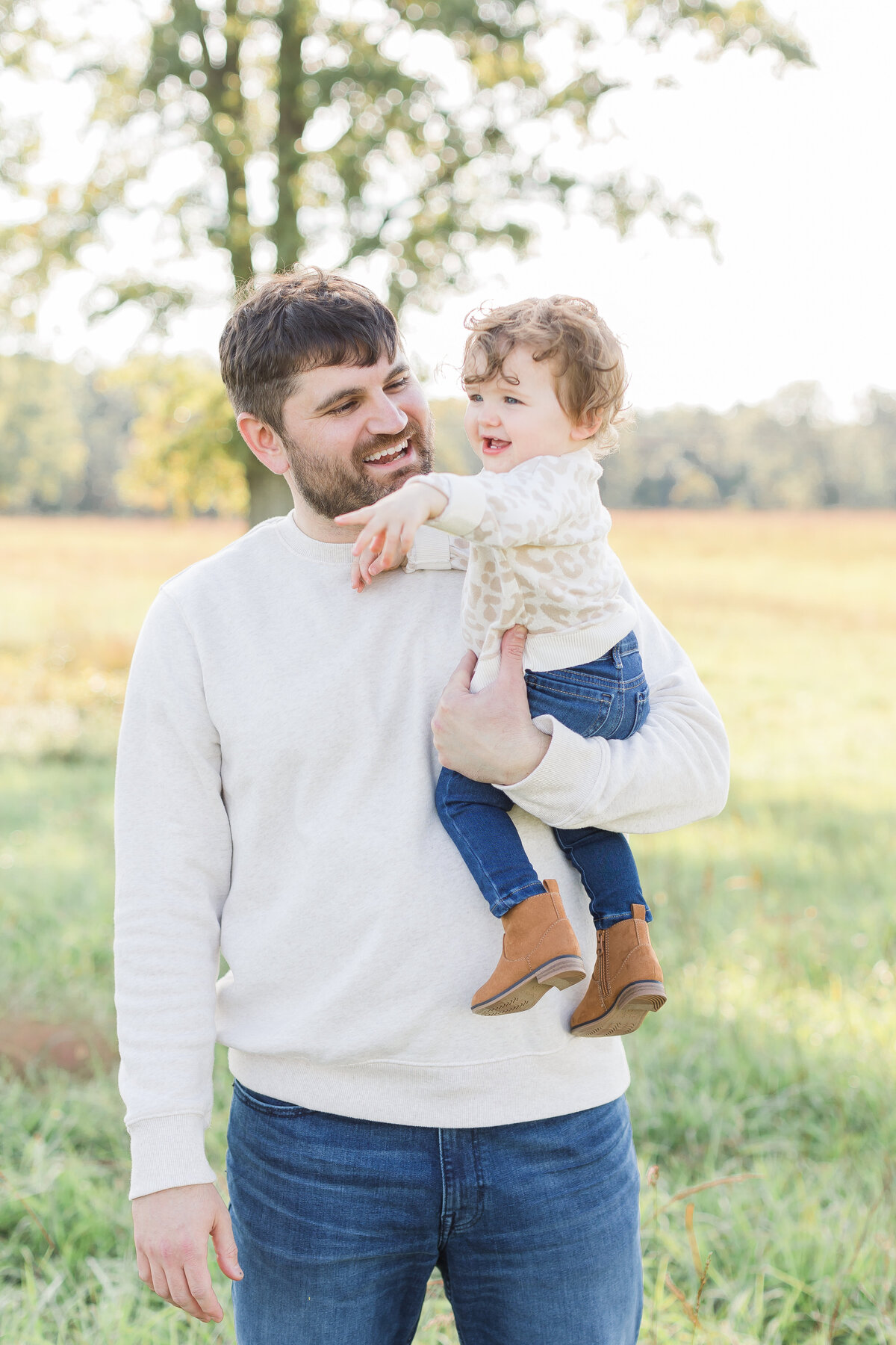 A Northern Virginia Family Photographer photo of a  father holding his smiling daughter outside in a field