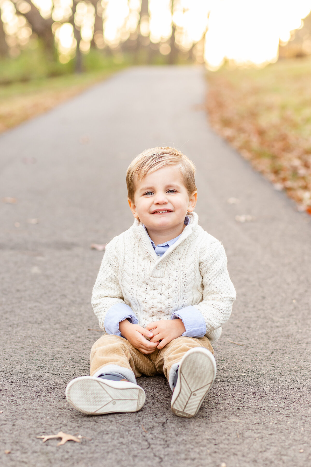 Little boy sitting on park pathway smiling