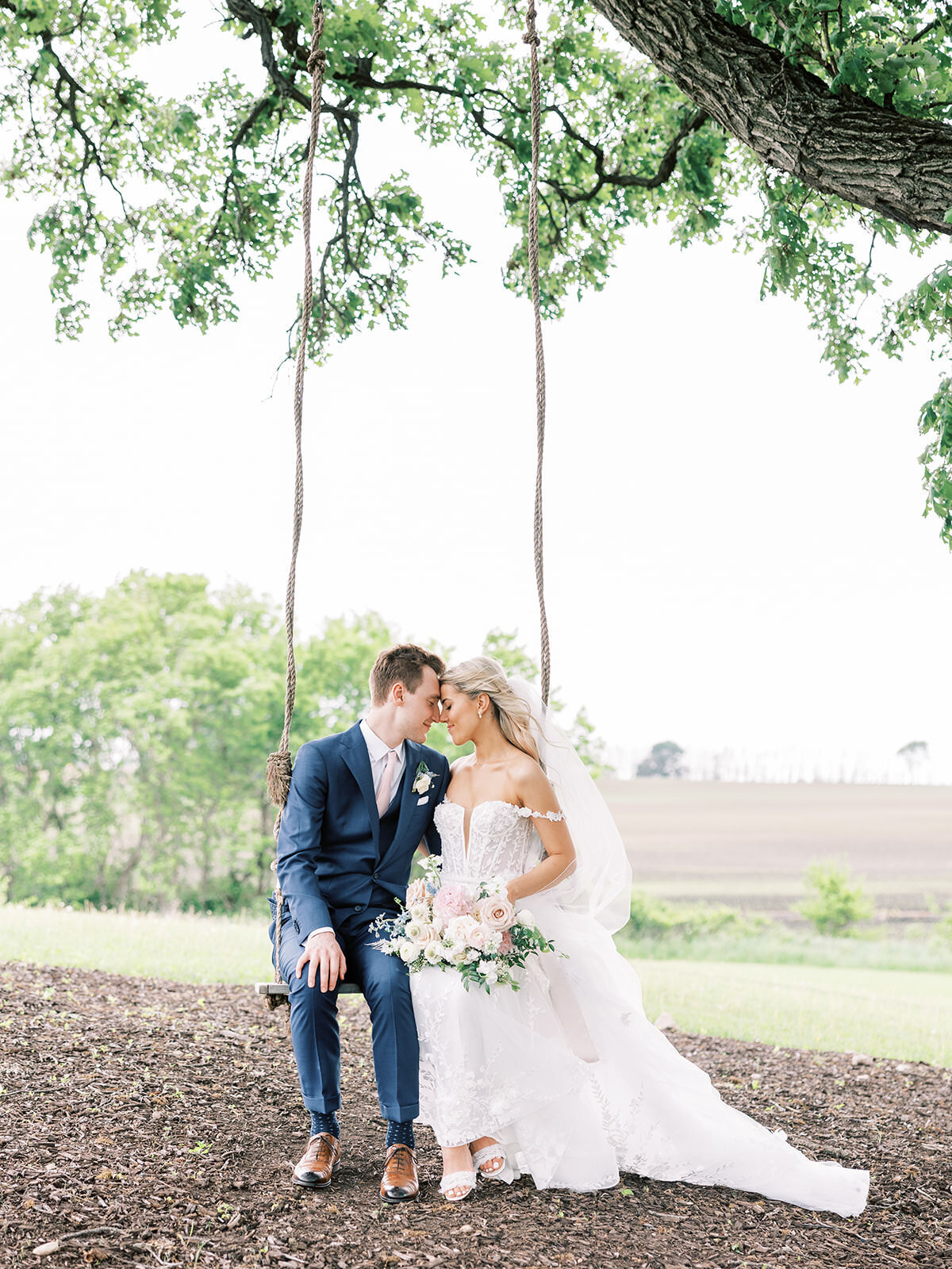 Bride and groom sit on swing under large oak tree