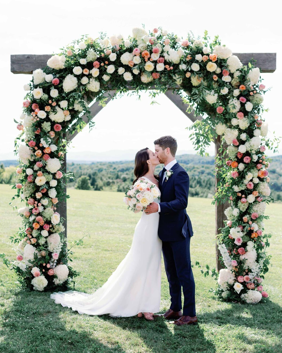 bride and groom kiss under floral arch by clayton floral at maquam barn and winery wedding