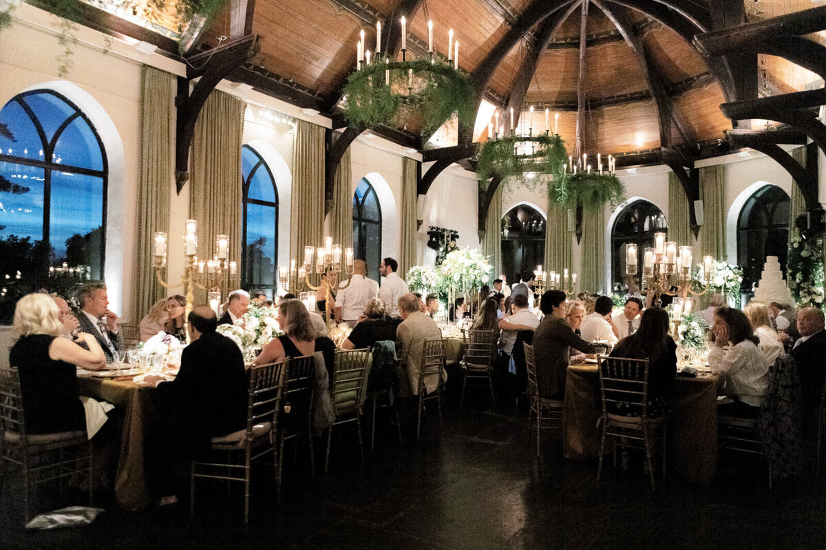 Guests are seated on bronze tables and chairs inside an elegant wedding reception room with candle chandeliers.