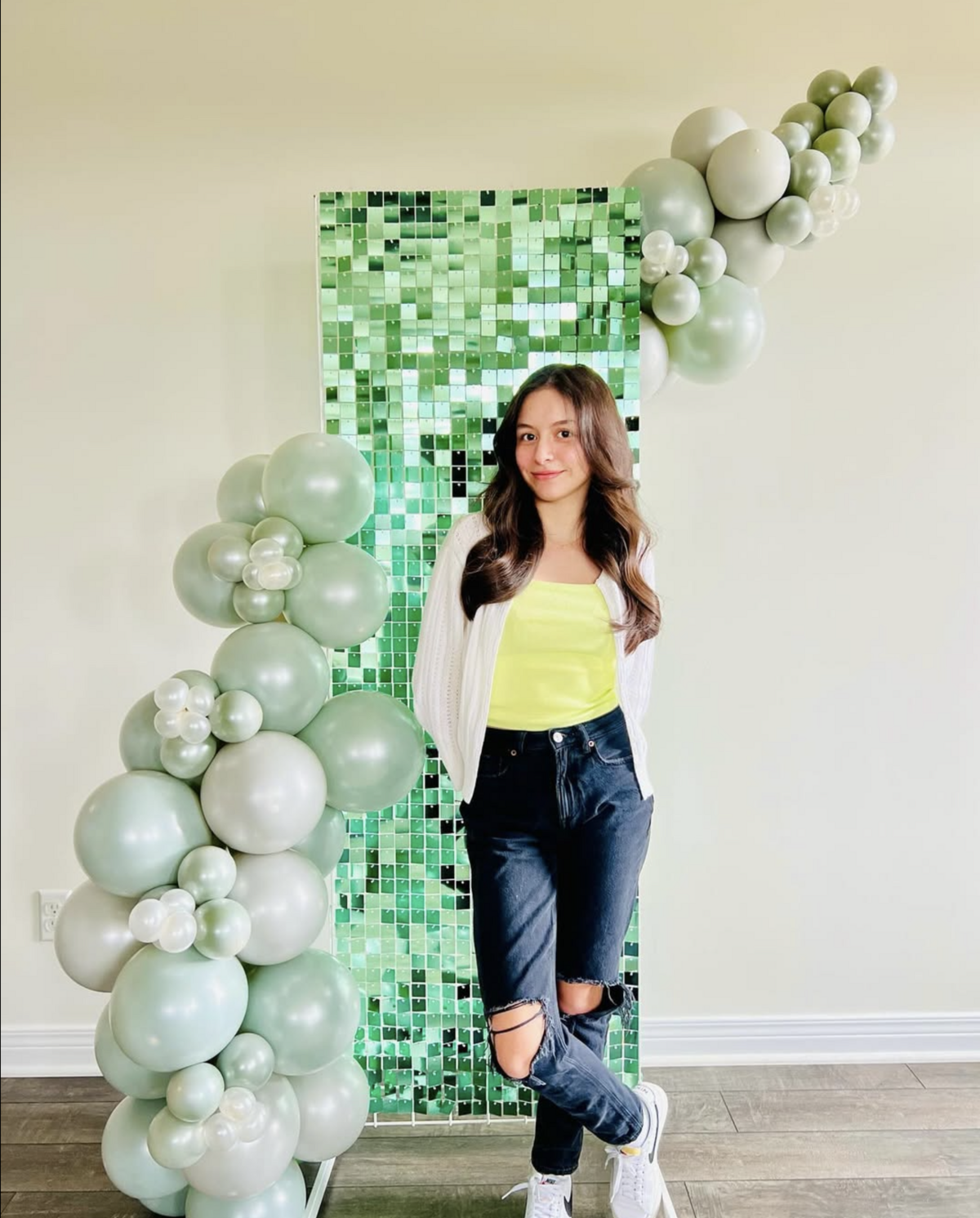 Sandra posing in front of a leafy green and white balloon installation for a stylish event.
